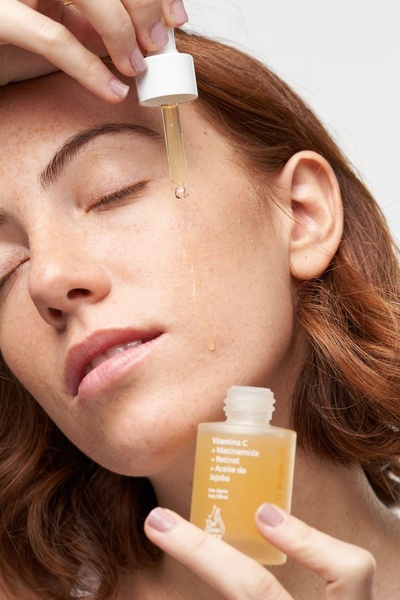 A close-up shot of a model applying a facial serum with a glass dropper, emphasizing product texture and skin health.